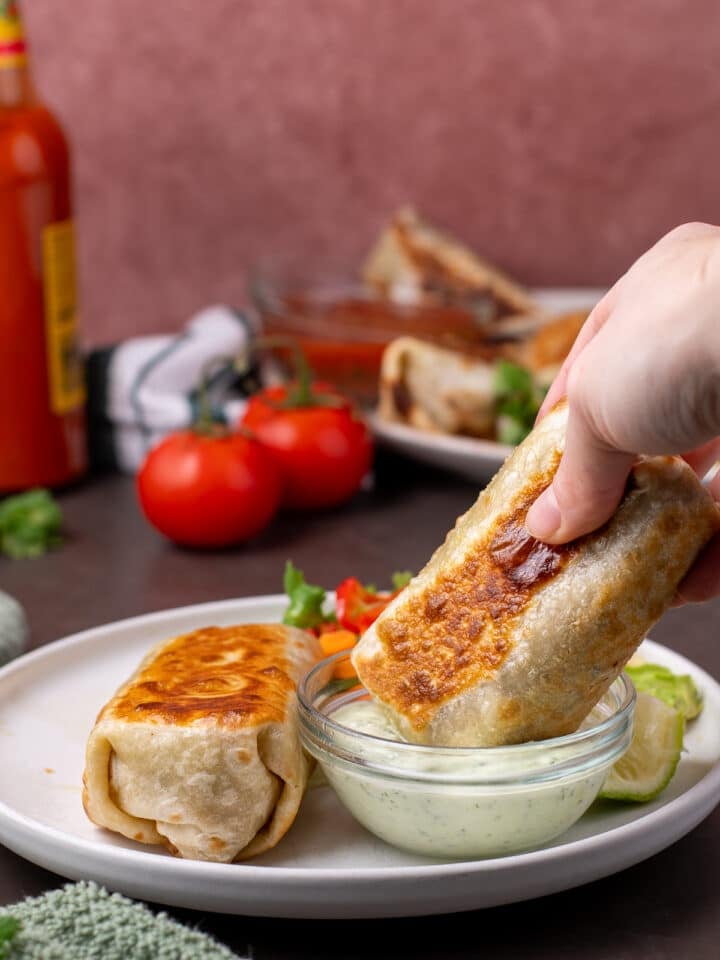 hand dunking a burrito into cilantro yogurt sauce