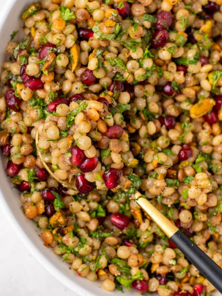 Close up of pearl couscous pilaf with pistachios, pomegranate and chopped fresh herbs
