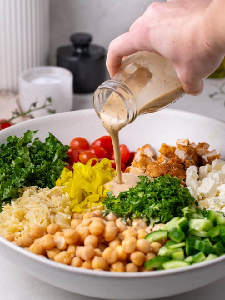 hand pouring creamy balsamic vinaigrette on a large bowl of salad