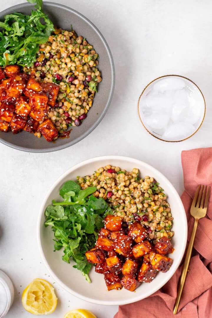two bowls of apricot harissa tofu with couscous pilaf and arugula for a plant-based dinner