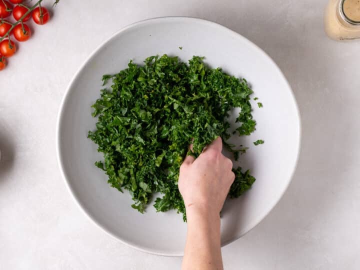 hand massaging kale in a large white bowl