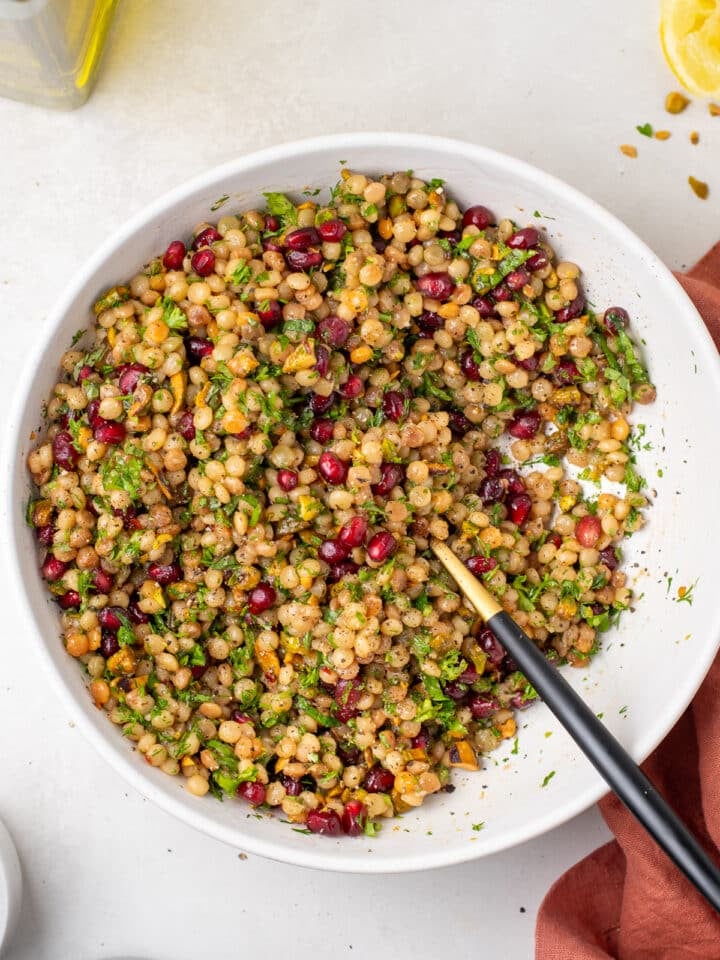 Tossed couscous pilaf with pistachios, pomegranate and fresh herbs in a white serving bowl