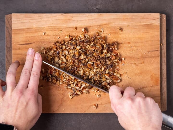 hands using a knife to chop together raw sugar, pecans and date