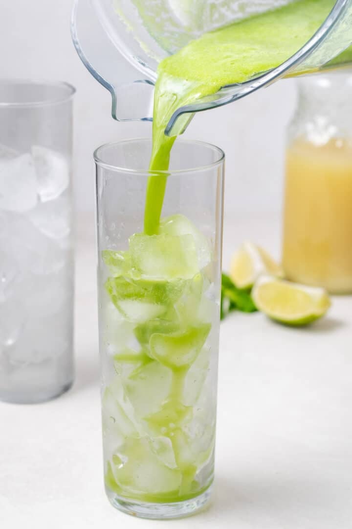 pouring cucumber mint mixture into a glass with ice