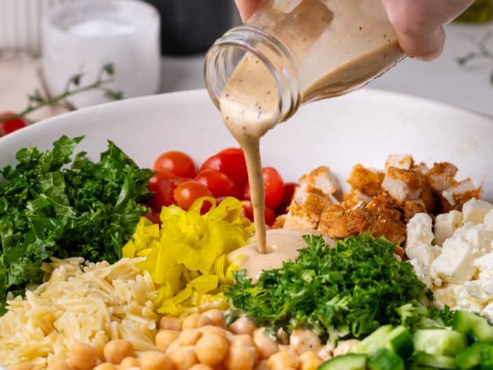 hand pouring balsamic dressing on salad