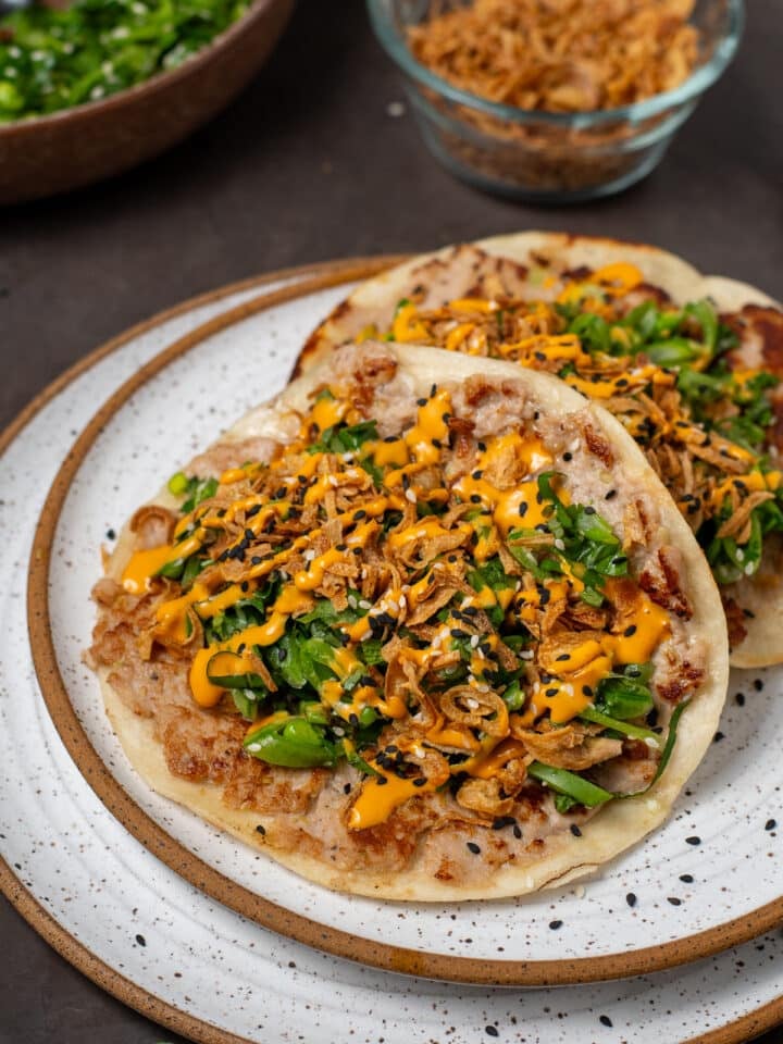 Seared ahi tuna smash tacos topped with snap pea herb salad, crispy shallots, sesame seeds, and spicy sriracha mayo on a plate