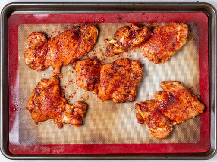 Seasoned chili lime chicken thighs arranged on a baking sheet lined with a silicone mat before roasting