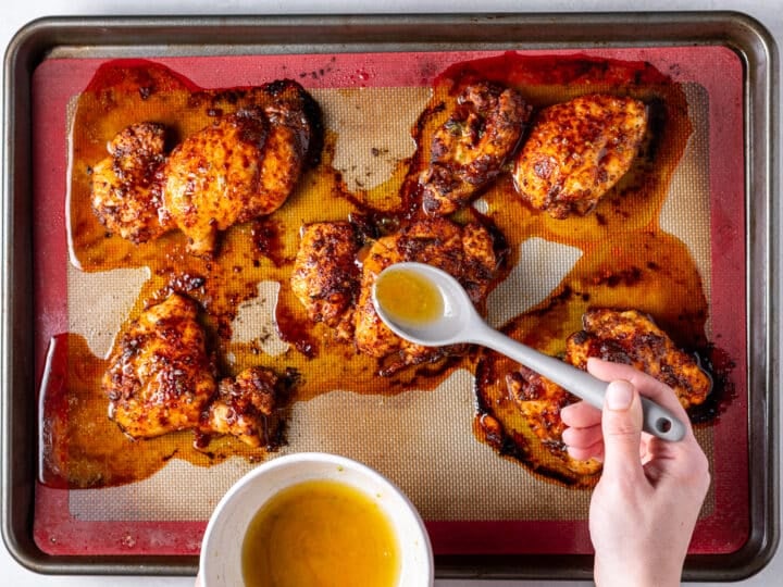 Spooning honey lime sauce over roasted chicken thighs on baking sheet during cooking