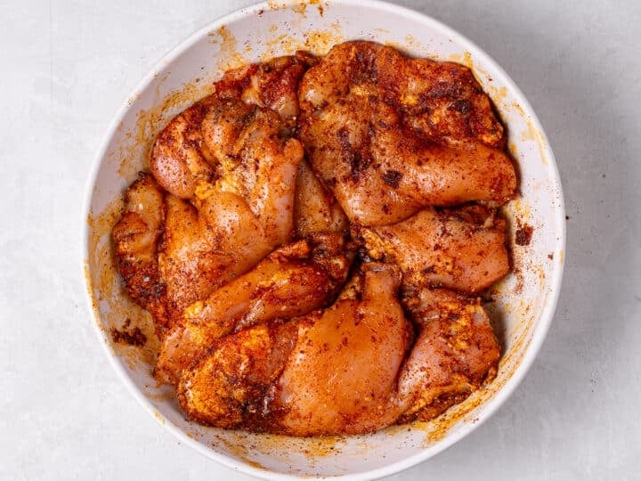 Mixing spices with raw chicken including paprika, chili powder, garlic powder, onion powder, salt and pepper