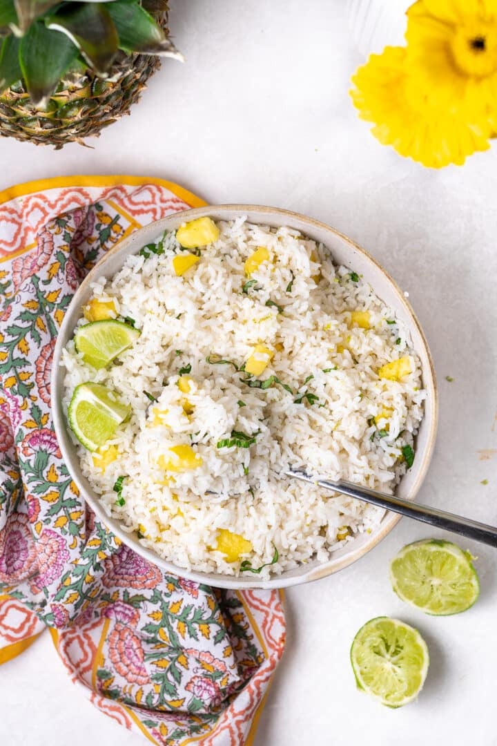 Overhead view of coconut rice with lime and Thai basil in a bowl with fresh pineapple and lime on the side