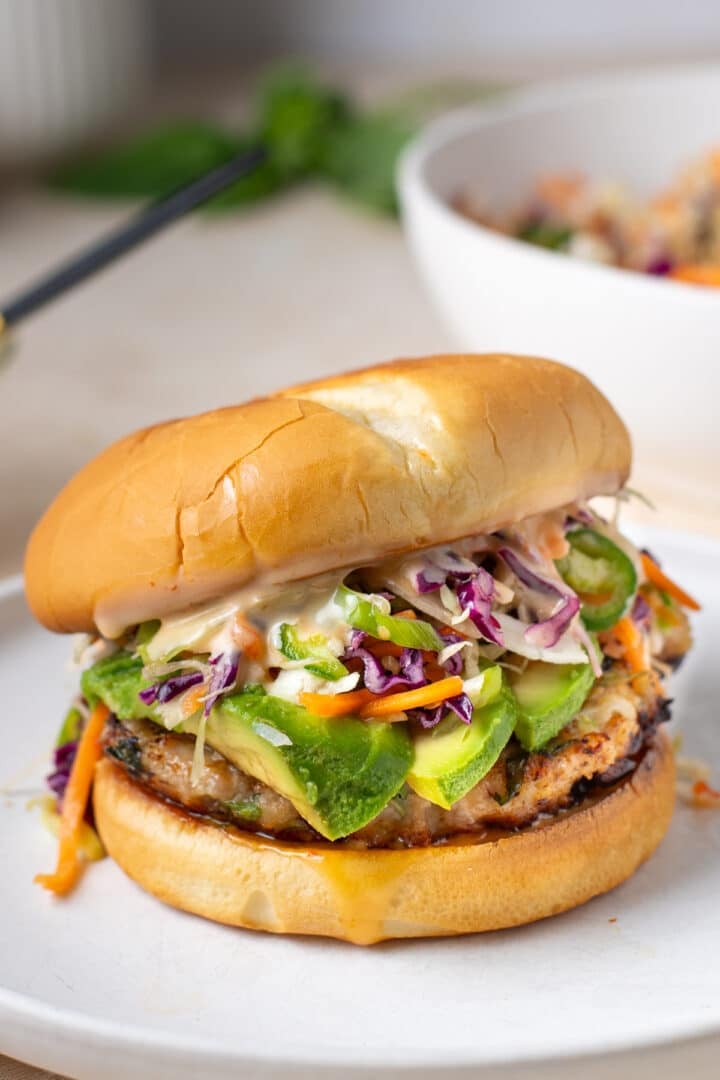 close up view of a ground chicken burger topped with avocado, slaw and creamy spicy sauce