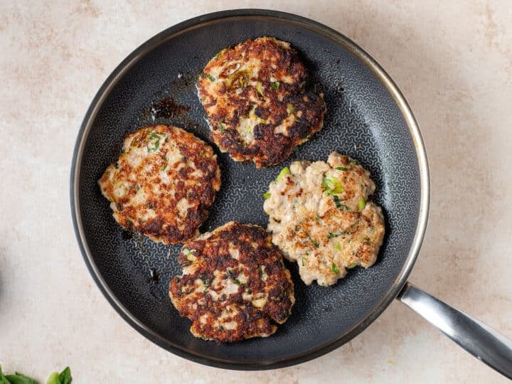 chicken patties cooking in a skillet with a golden brown crust