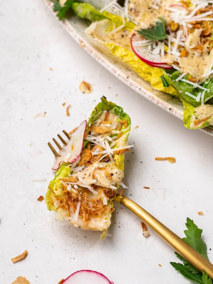little gem salad bite with Caesar vinaigrette, crispy shallots, parmesan, and radish on fork