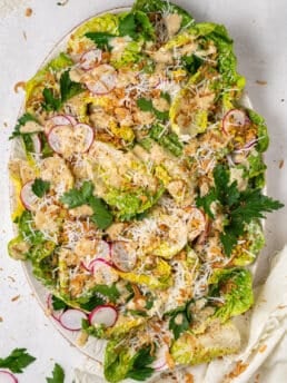 little gem salad recipe with Caesar vinaigrette, parmesan cheese, pistachios, and crispy shallots on platter