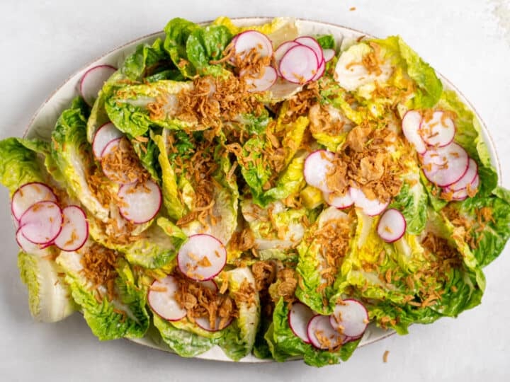 little gem salad topped with radishes and crispy shallots before adding remaining caesar vinaigrette