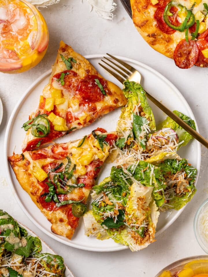 pepperoni pineapple pizza slices served with Caesar salad with parmesan cheese and crispy shallots