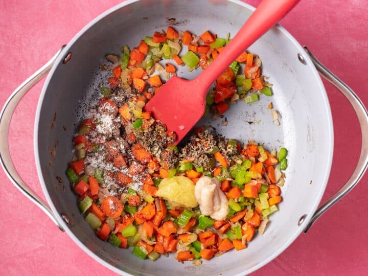 Sautéed vegetables in a pot with garlic, ginger, dried basil, red pepper flakes, salt, and pepper