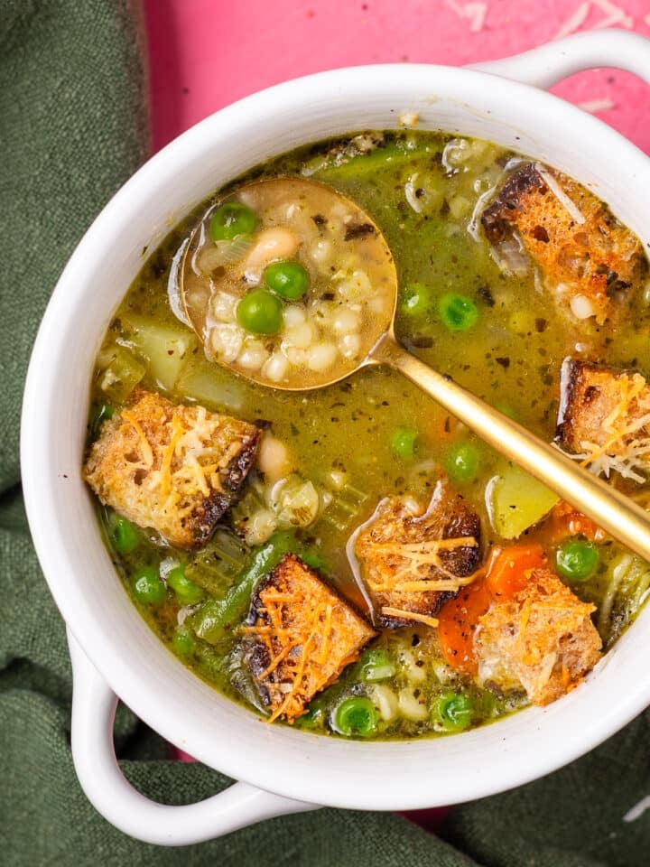 Close-up of minestrone soup with pesto, white beans, pearl couscous, peas, and parmesan croutons