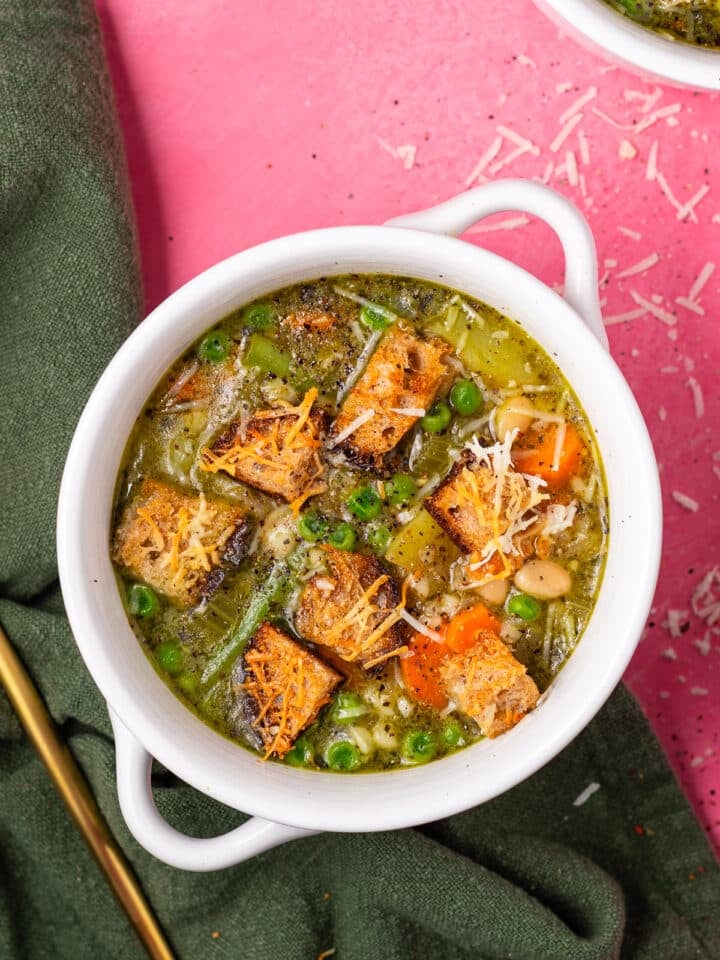 Bowl of minestrone soup with pesto, pearl couscous, white beans, carrots, peas and crispy parmesan garlic croutons