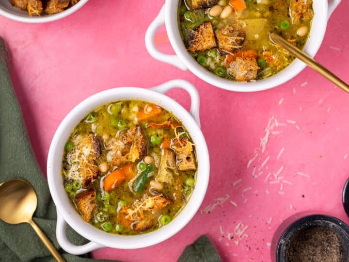 Wide overhead view of two bowls of minestrone soup with pesto and homemade croutons