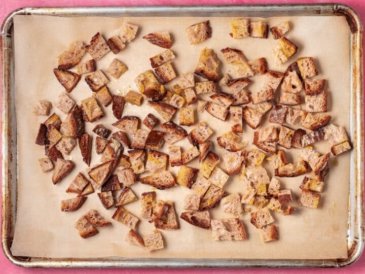 Partially baked sourdough croutons spread on a parchment-lined sheet pan