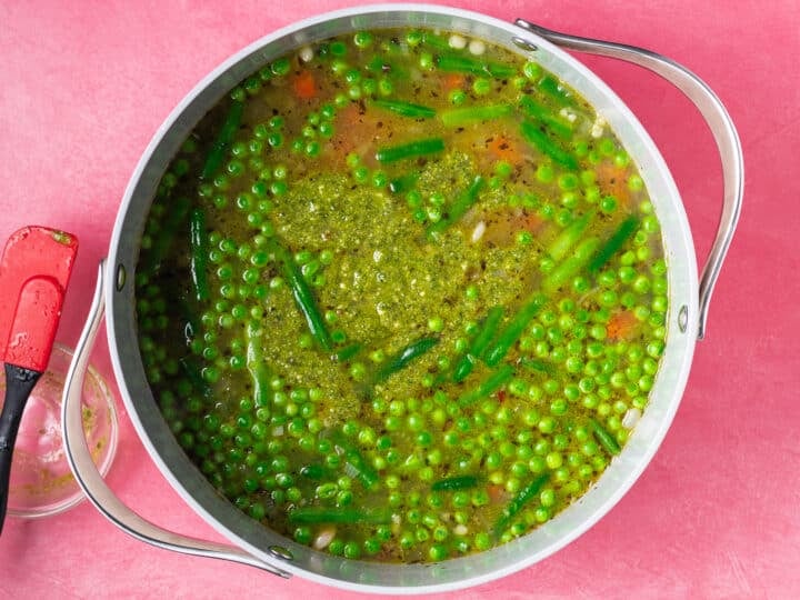 Spring vegetable soup with pesto stirred in, peas and green beans visible throughout the pot