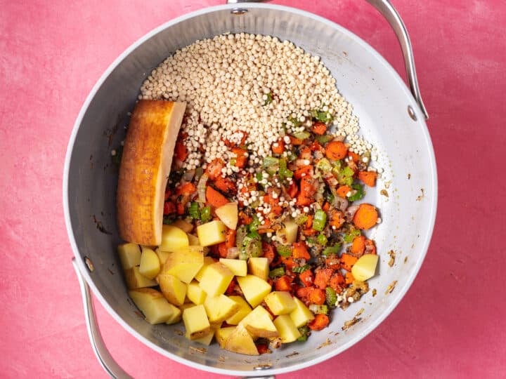 Pearl couscous, diced potatoes, and a parmesan rind added to sautéed vegetables in a soup pot