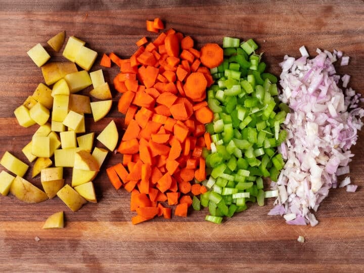 Chopped Yukon gold potato, carrots, celery, and shallots lined up on a cutting board