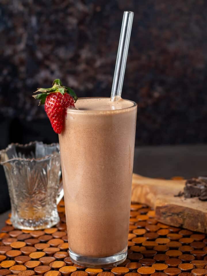 Iced chocolate coffee protein smoothie blended with banana and cacao, served in a tall glass with a straw