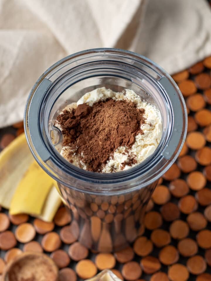 Ingredients for mocha protein shake in blender cup with protein powder and cacao on top