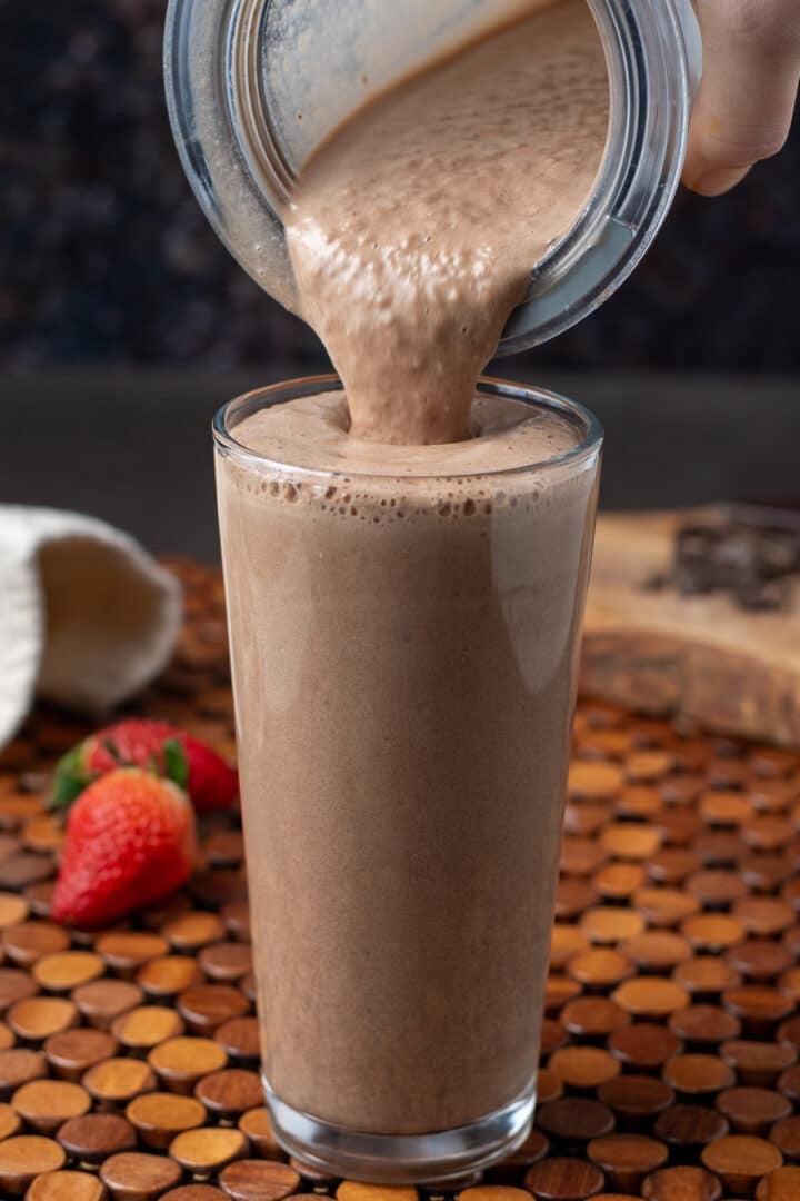 Pouring mocha protein smoothie into tall glass