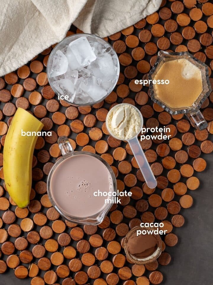 Ingredients for a mocha protein shake including banana, espresso, chocolate milk, protein powder, cacao powder, and ice