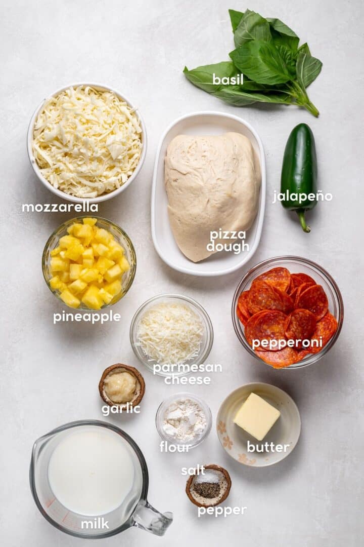 Ingredients for pepperoni pineapple pizza with creamy garlic sauce, including pizza dough, mozzarella, pepperoni, pineapple, jalapeño, basil, parmesan, garlic, milk, butter, and flour