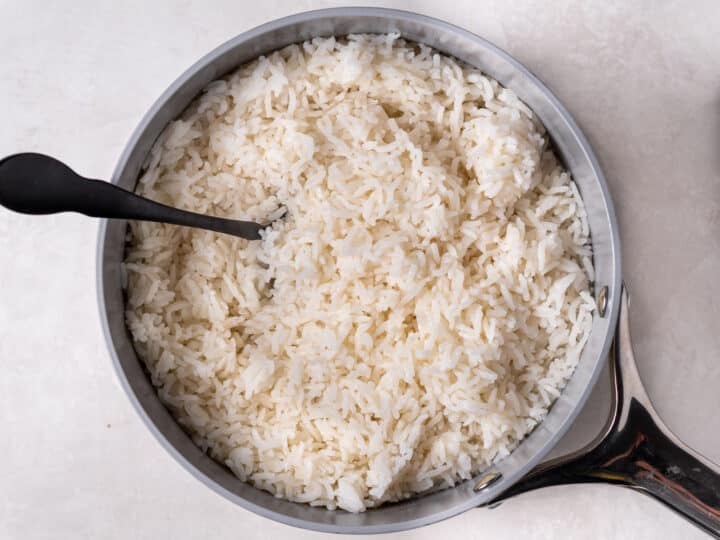 Fluffing cooked coconut rice in a saucepan with a fork after steaming