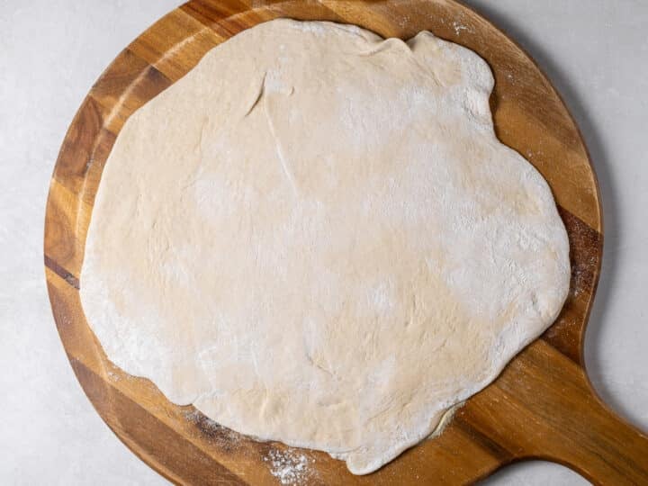 Fresh pizza dough stretched into a thin round on a wooden pizza peel dusted with flour