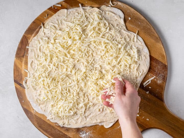 Shredded mozzarella cheese sprinkled over garlic sauce on pizza dough