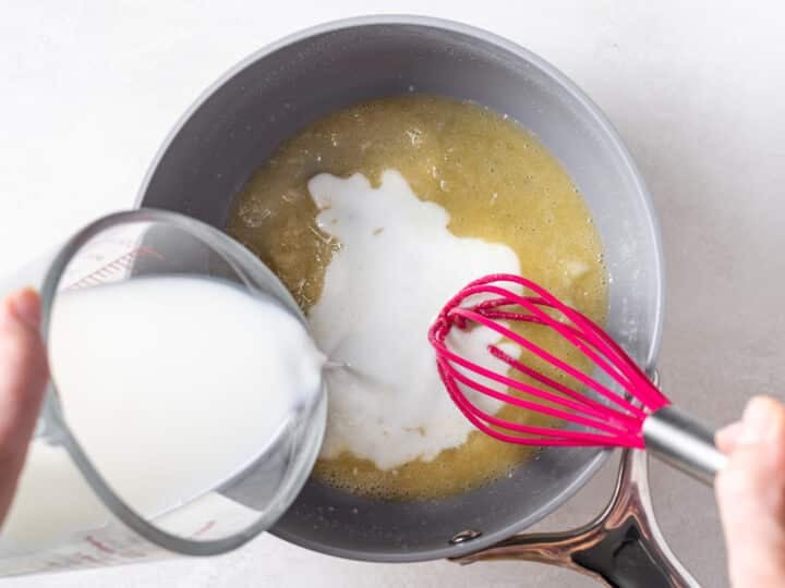 Milk being poured into garlic roux while whisking to create creamy garlic sauce
