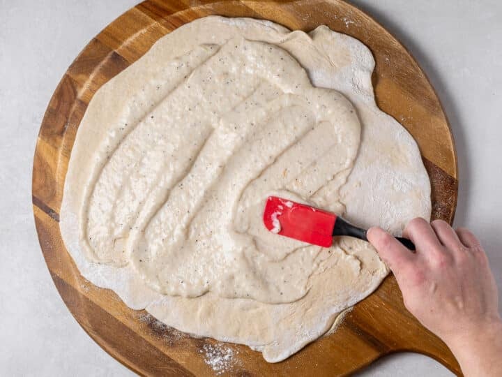 Creamy garlic sauce spread evenly over pizza dough using a spatula