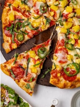 Pepperoni pineapple pizza with jalapeño slices and fresh basil, showing a slice being pulled away with melted mozzarella and diced pineapple