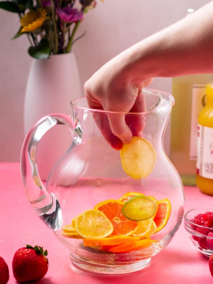 hand putting citrus slices in a pitcher