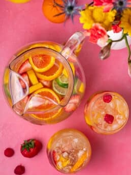 pitcher and two glasses filled with refreshing springtime sangria with mango, raspberries, strawberries and citrus fruits