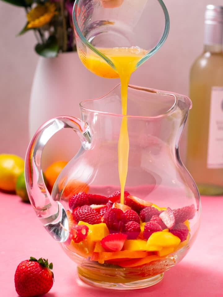 pouring pineapple juice over fresh fruits in a pitcher