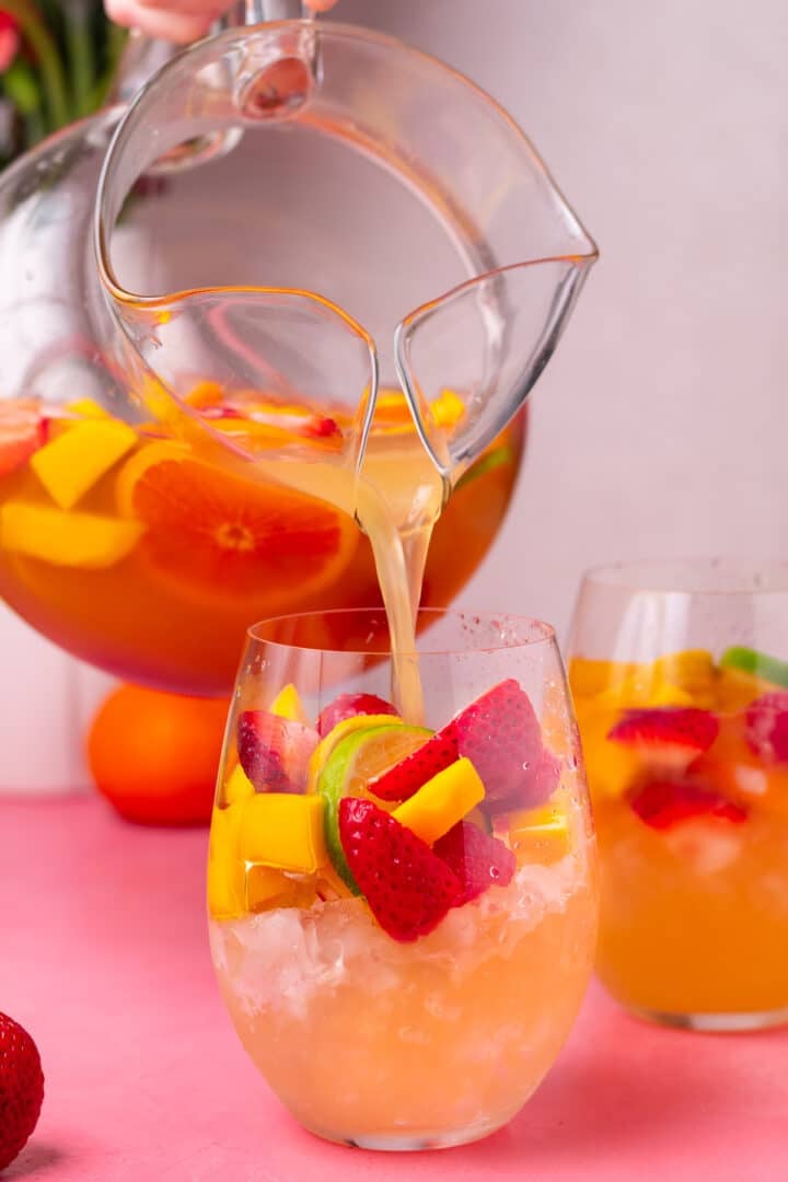 hand pouring a pitcher of white sangria into a wine glass