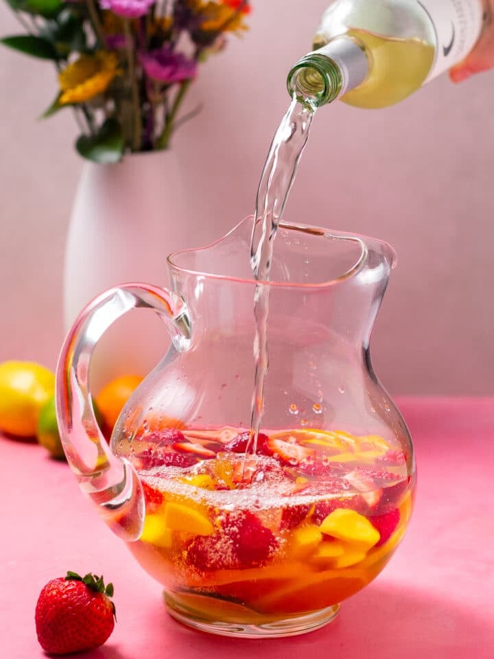 hand pouring a bottle of white wine into a pitcher