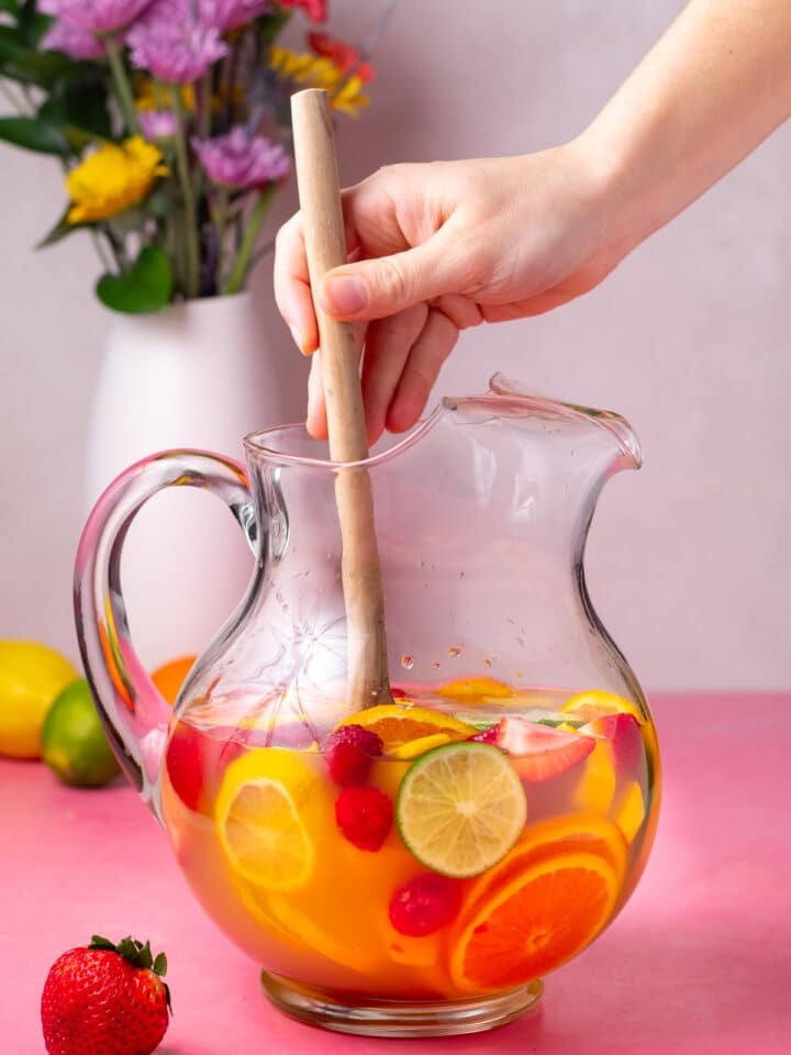 hand using a wooden spoon to stir sangria and fruits