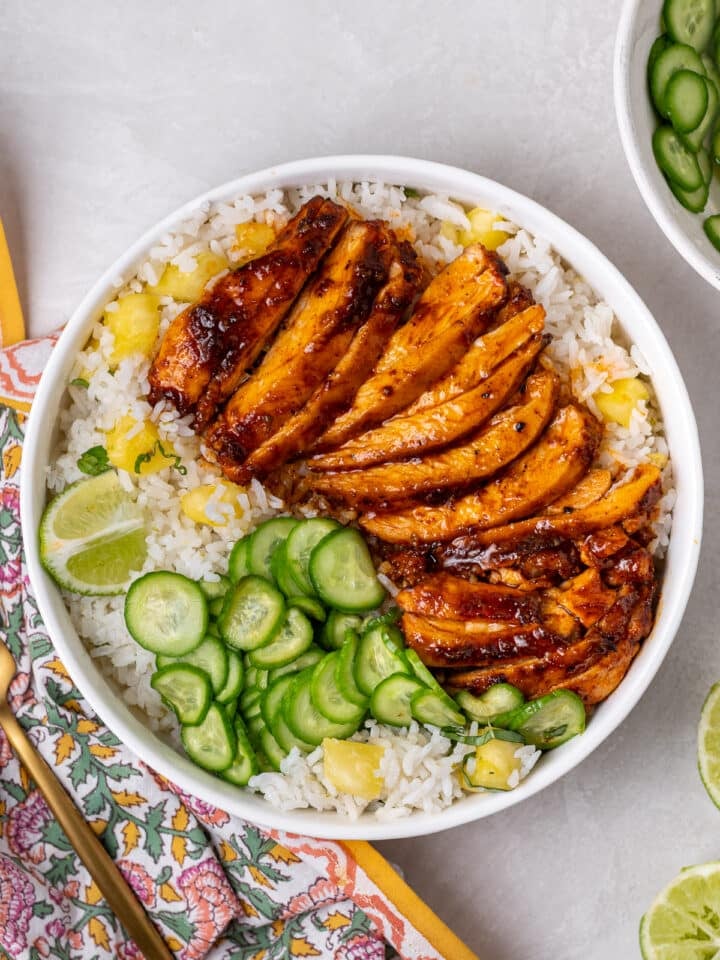 Lime coconut rice bowl with pineapple, sliced chicken, cucumbers, and lime wedges