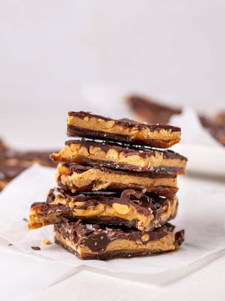 Stacked pieces of date bark with chocolate, peanut butter, chopped peanuts, and flaky sea salt on parchment paper