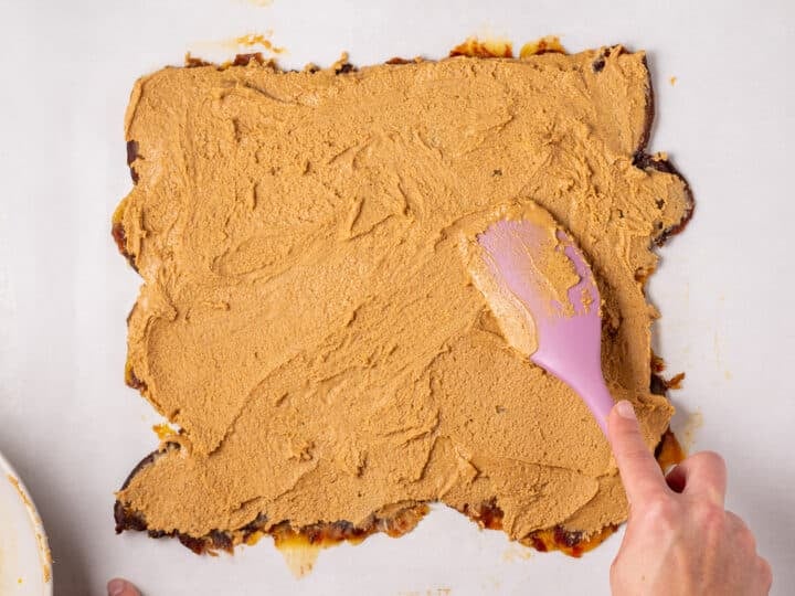 Peanut butter mixture being spread over the flattened date layer with a pink spatula