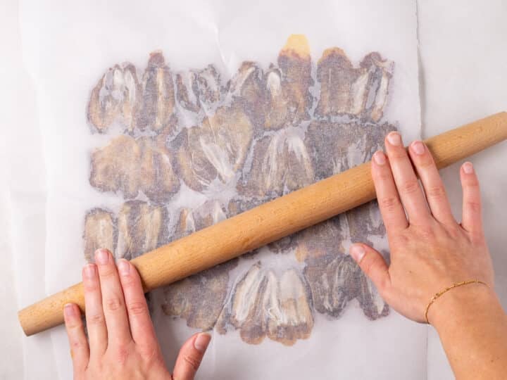 A rolling pin flattening dates between two sheets of parchment paper