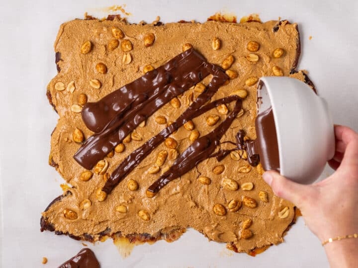 Melted chocolate being poured over the peanut butter and peanut layer